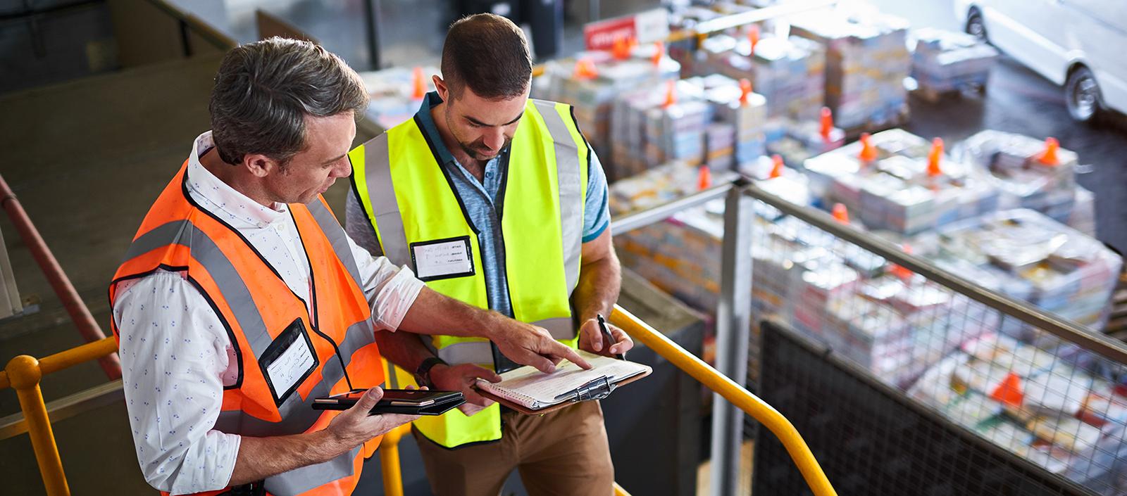 Shot of two warehouse workers standing on stairs using a digital tablet and looking at paperwork.