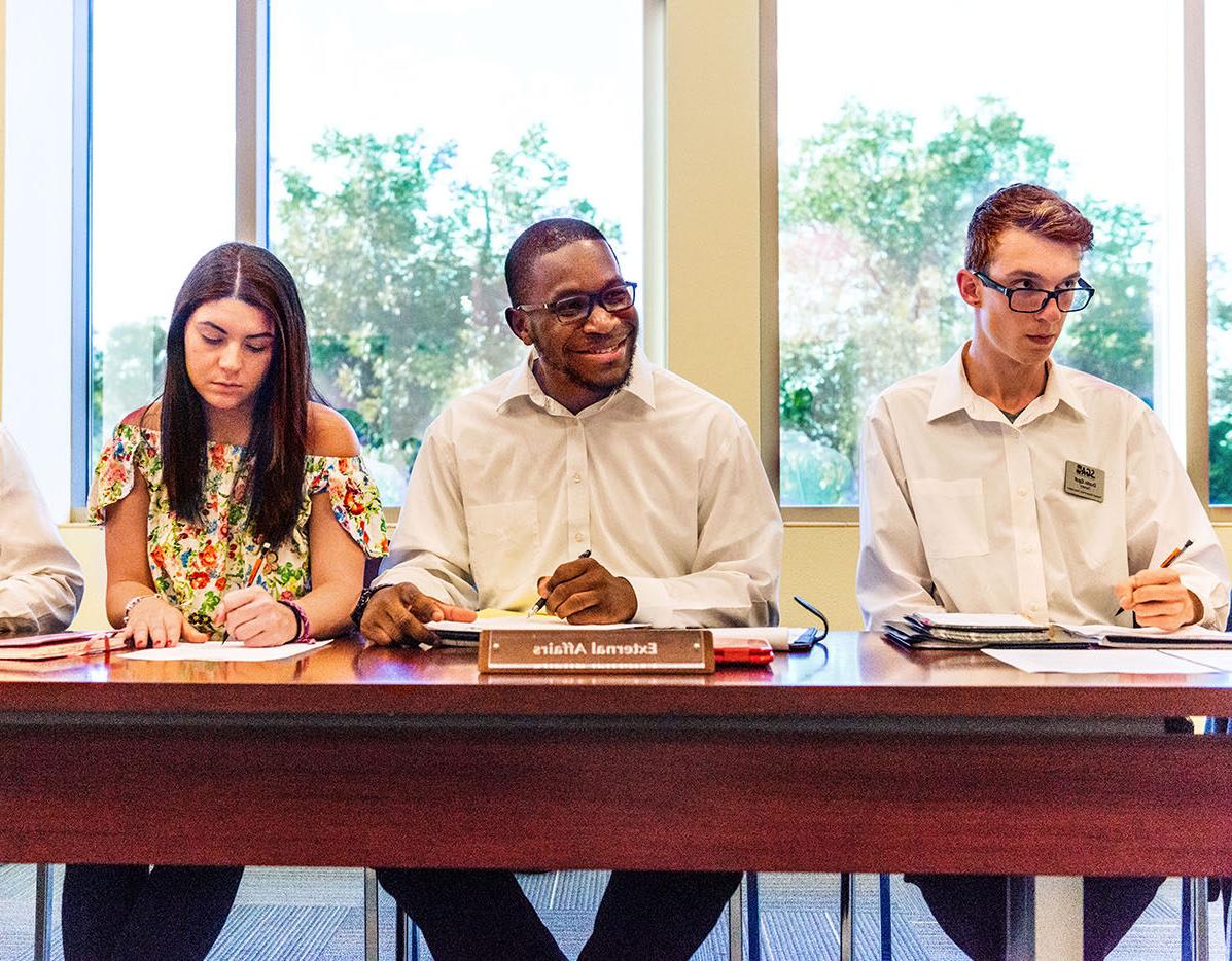 Two male students and one female student sitting at a table during a student government meeting.