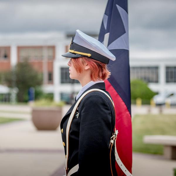 A female soldier standing to the right with a flag beside her.