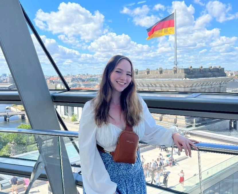 A young female in a glass bridge with a building behind her displaying the german flag.