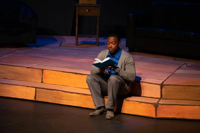 a male student sitting and reading a book in a play